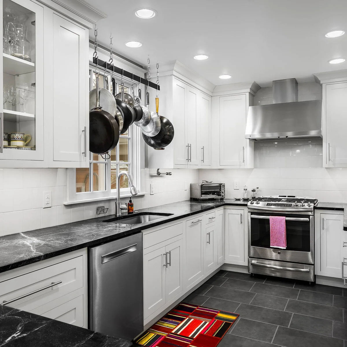 White kitchen with a hanging pan rack above the sink window and dark counters
