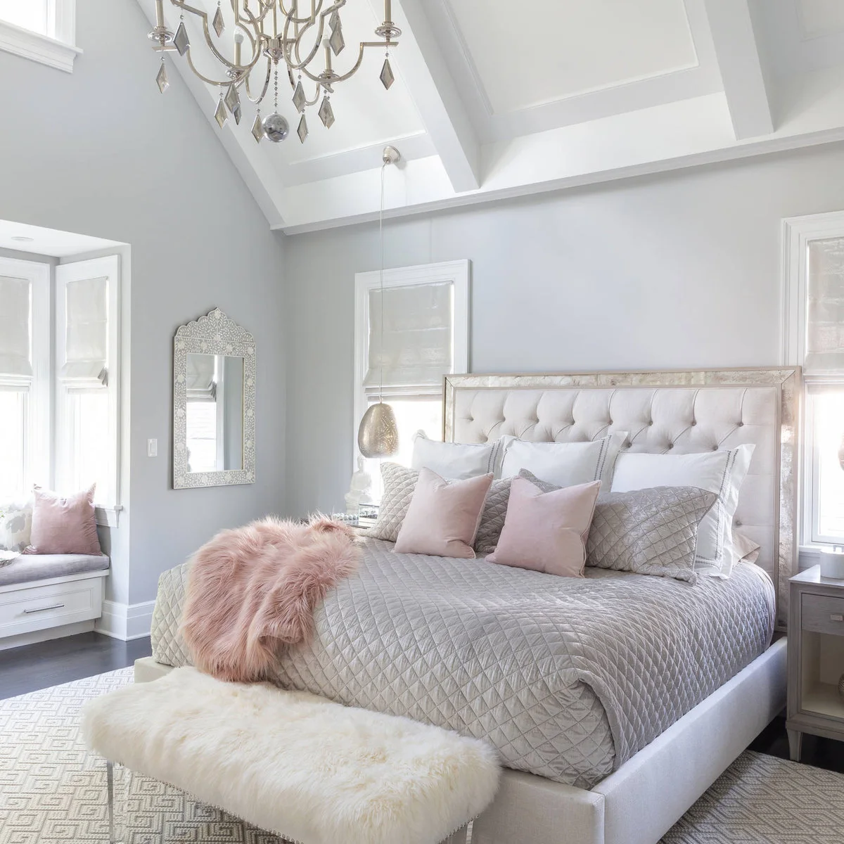 Pale grey bedroom with a quilted grey coverlet, pink cushions and a light upholstered bench