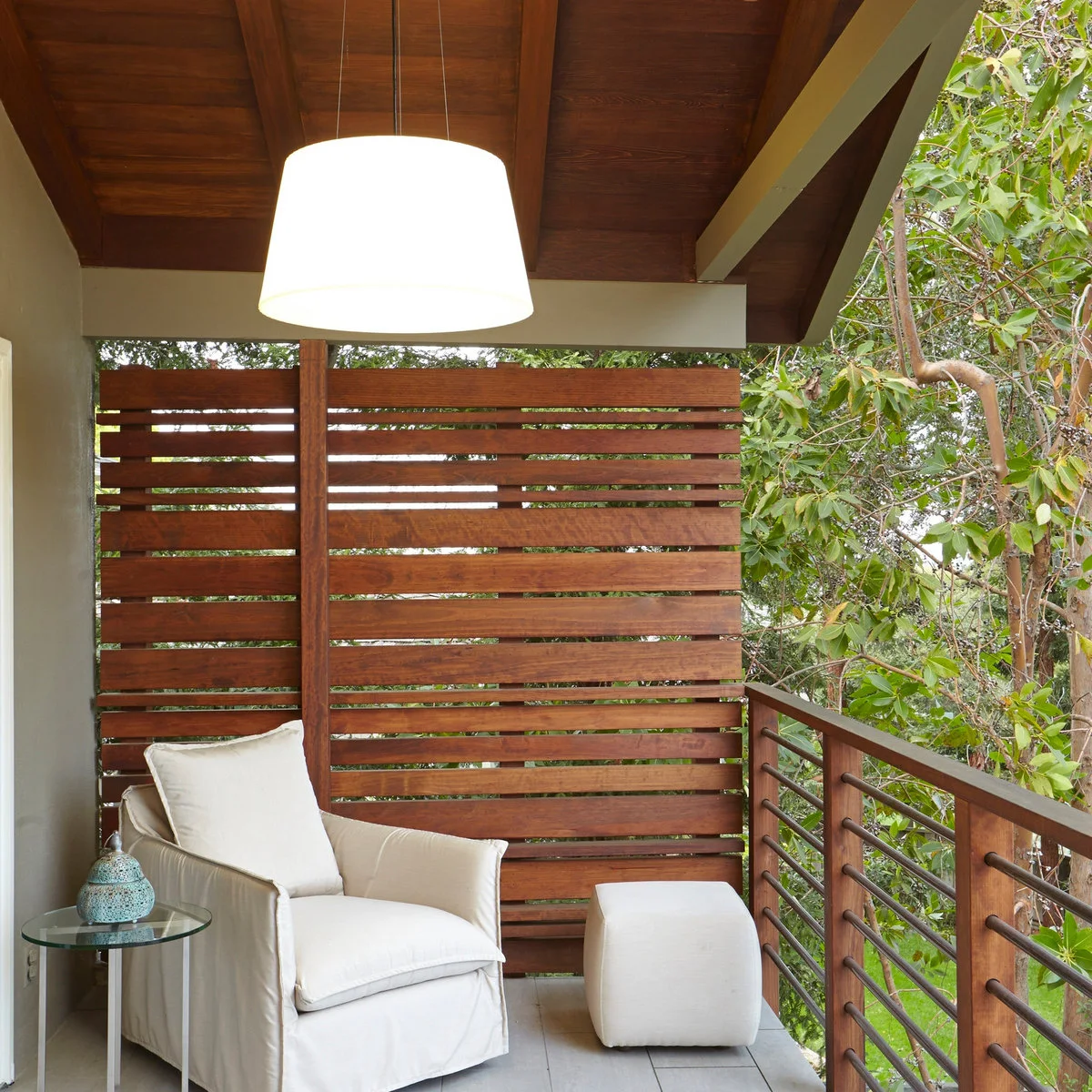 A horizontal timber panel stands behind a pale chair on a covered elevated outdoor space