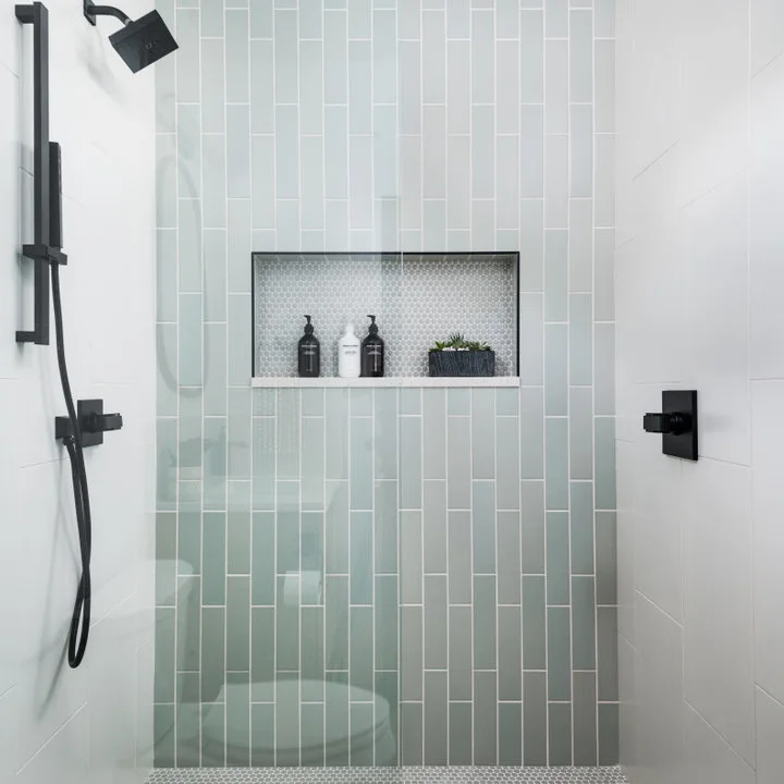 A pale green vertical-tiled shower wall contains a horizontal niche, with black fittings and white side walls.