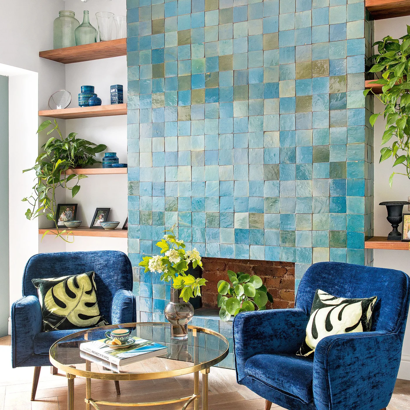 Blue-green square tiles cover a chimney breast between wooden shelves and two blue armchairs