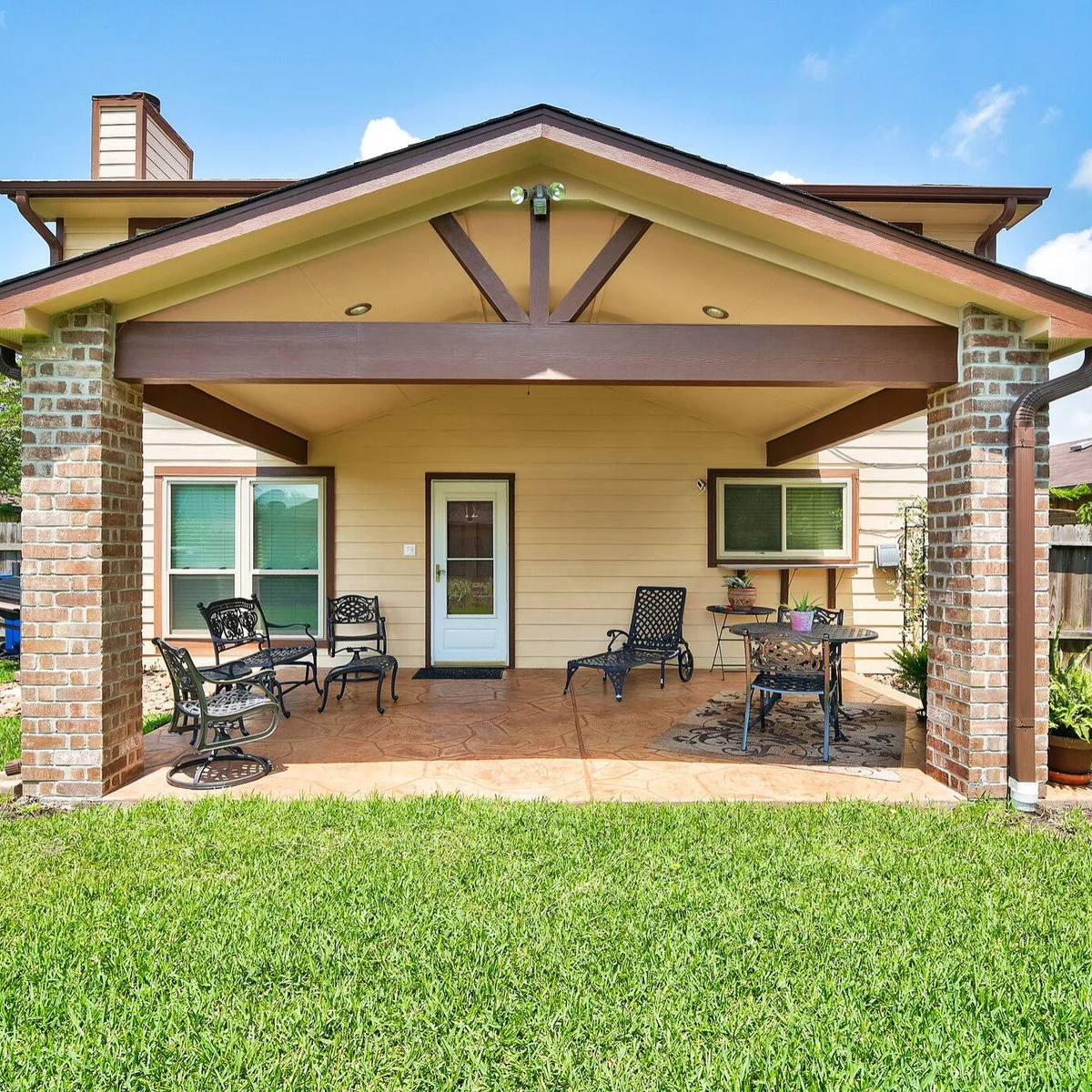 A compact gabled patio with brick columns contains two small table groups and an open route to the back door.