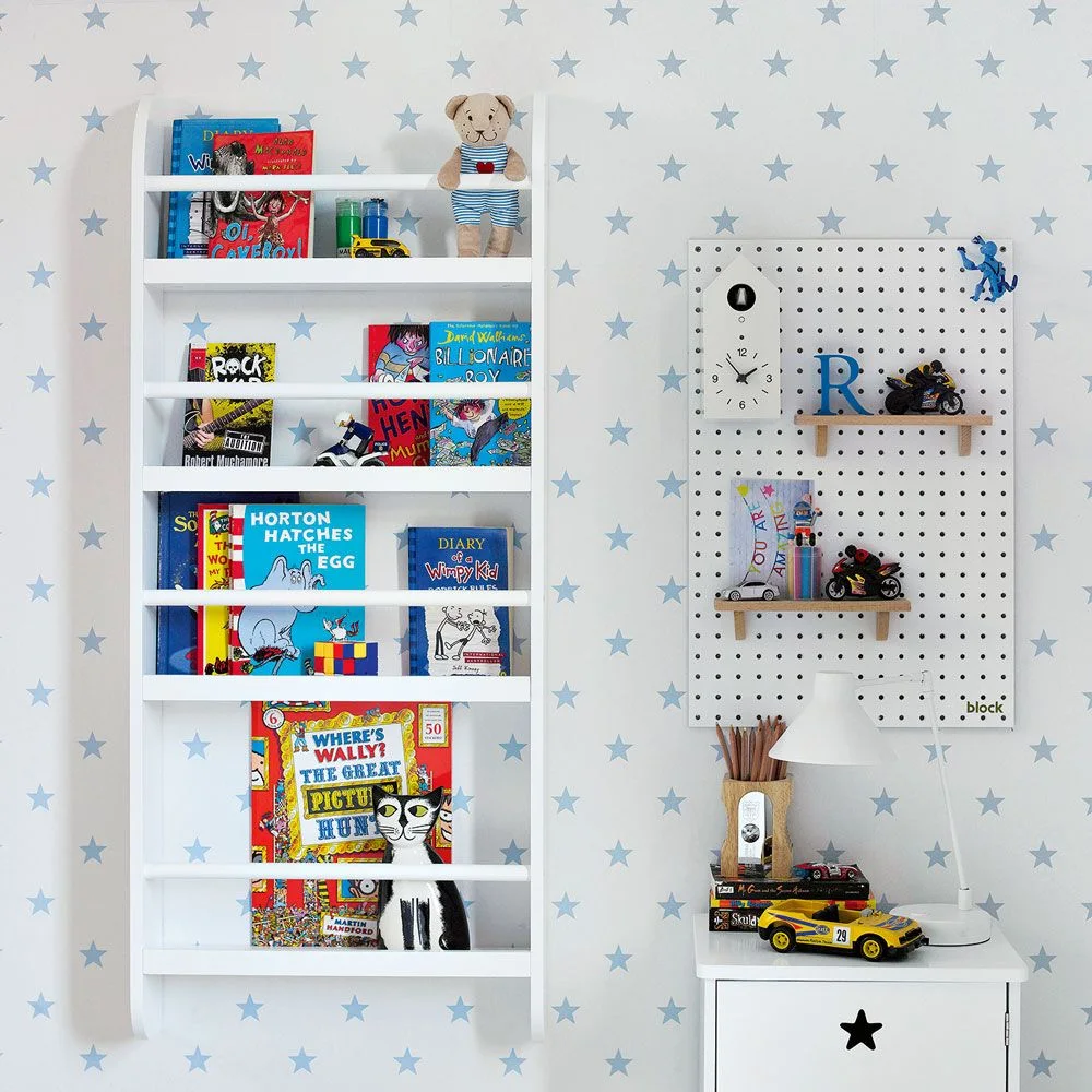 White wall book rack beside a pegboard displaying toy vehicles and a small cabinet