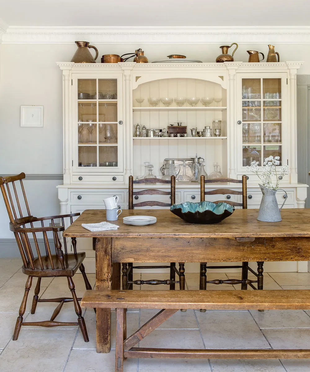 A pale dresser with glass upper doors stands behind a wooden dining table