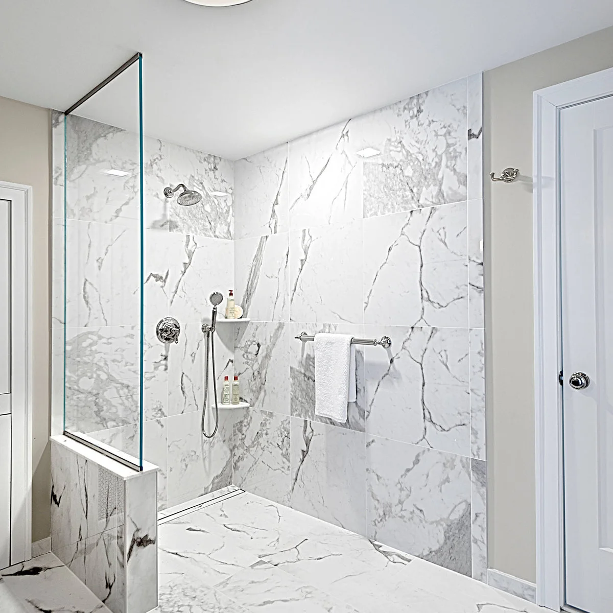 A clear screen rises above a low veined white partition beside a broad shower opening and a rear linear drain.