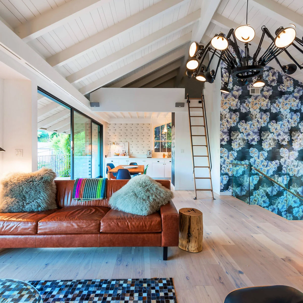 Large blue floral wallpaper covers a tall wall beside a brown sofa in an open living and kitchen space.