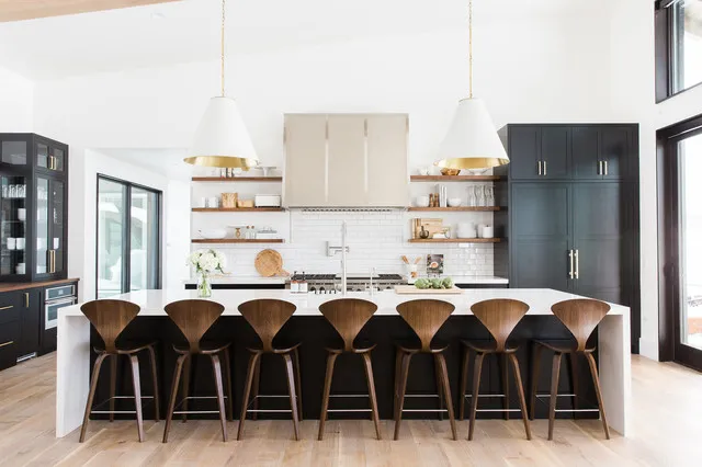 A long black island faces a row of curved timber stools in a bright kitchen.