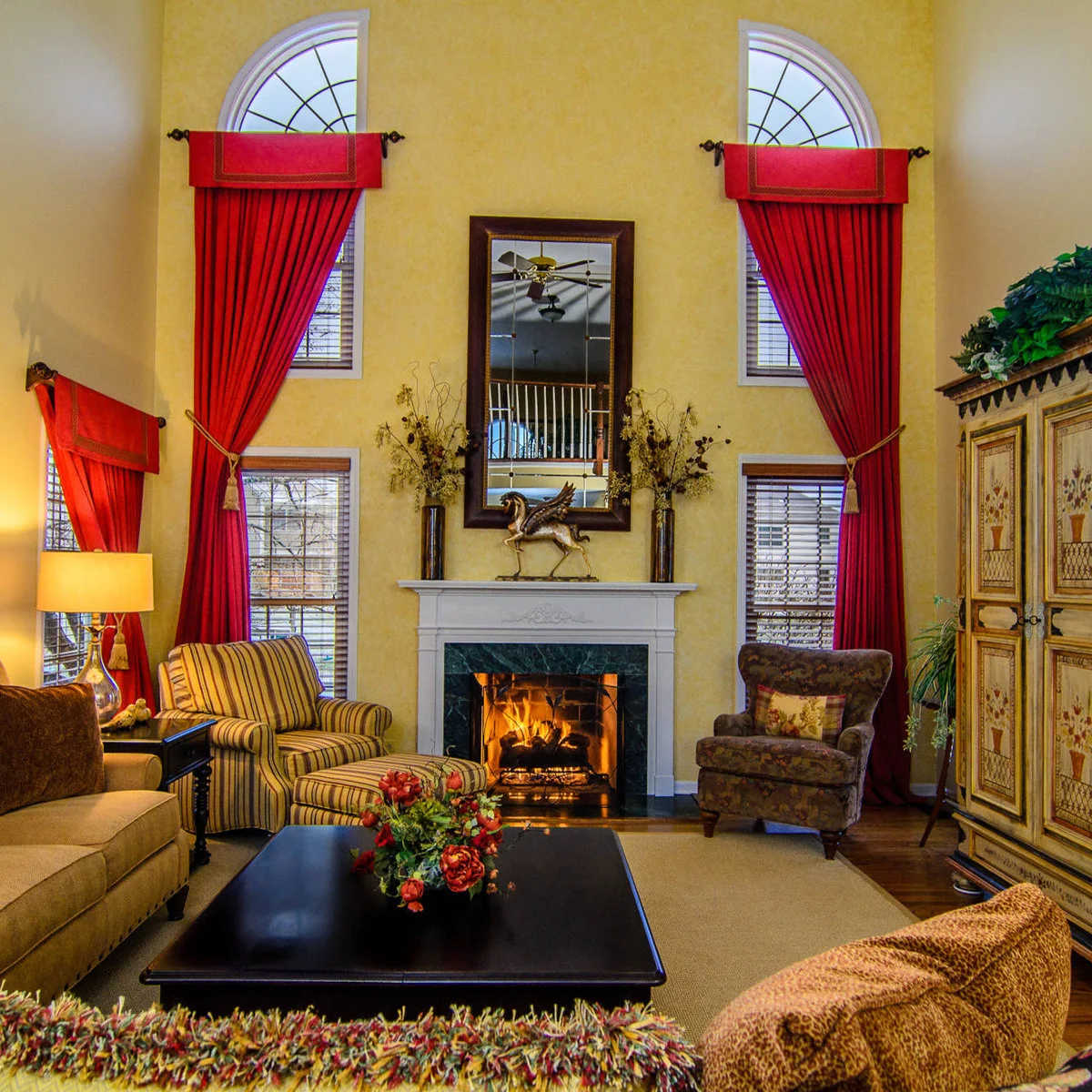 Tall living room with yellow walls, long red curtains, striped seating and a white fireplace surround