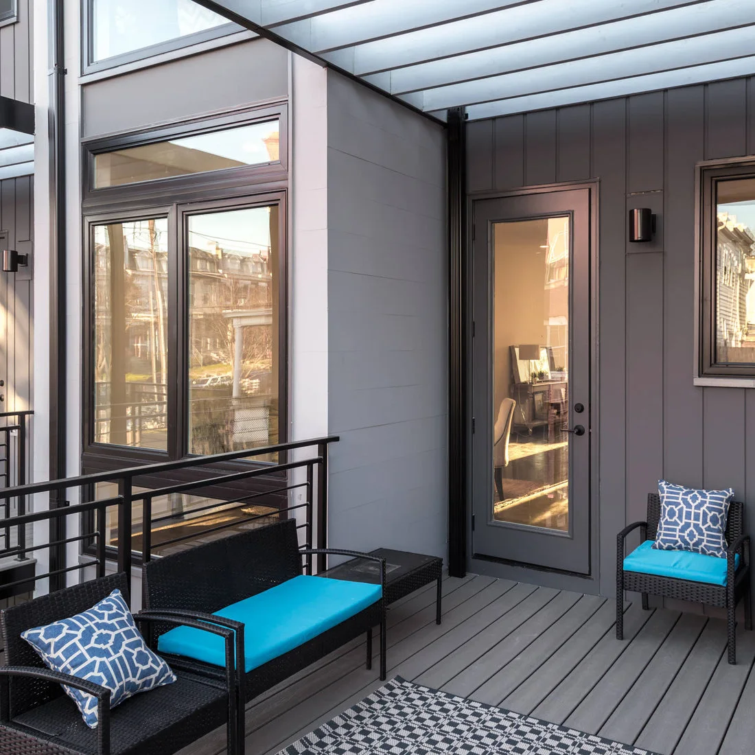 A dark loveseat and armchair with turquoise cushions face an open area on a gray balcony