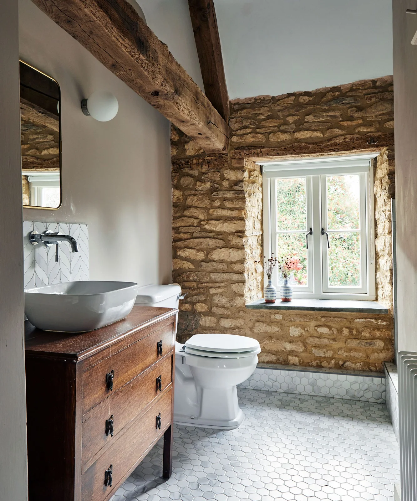 A wood drawer washstand and bowl basin beside rough masonry and exposed timber beams