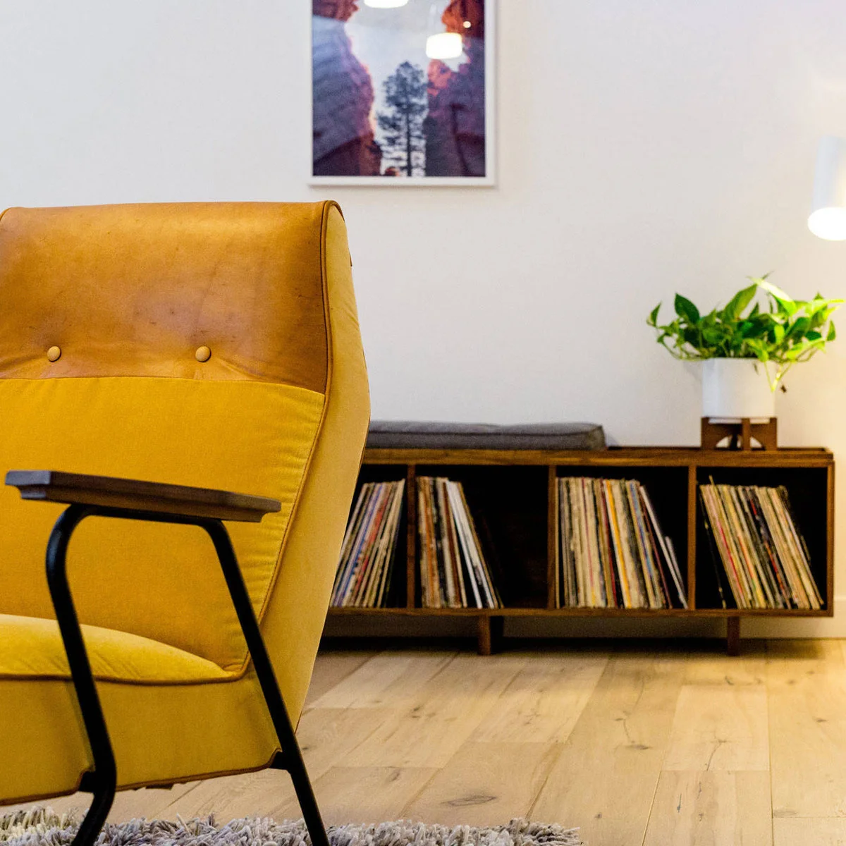 Mustard high-back chair with dark arms beside a low record cabinet, white wall and framed photograph