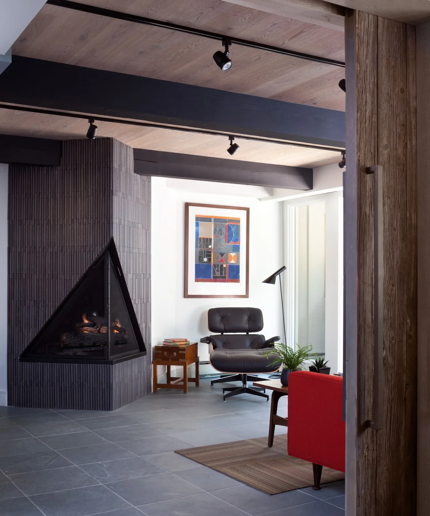 Black triangular corner fireplace against dark vertical panels beside a black chair and framed artwork.