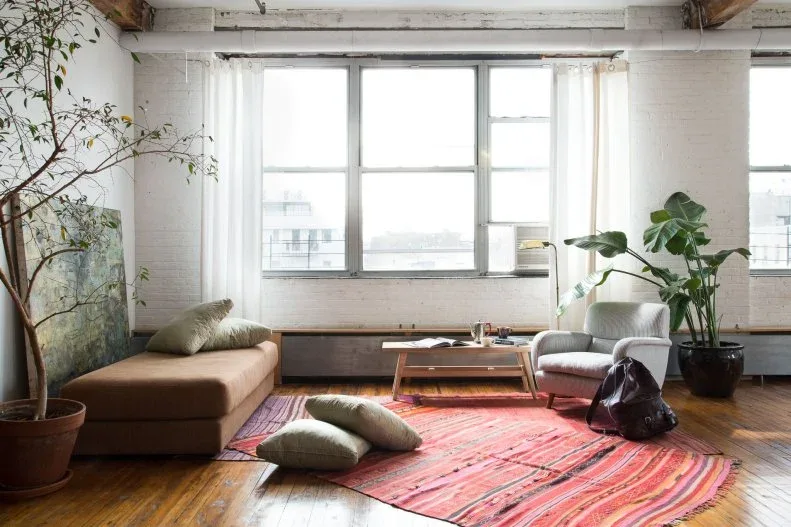 Loft sitting area with a red striped rug, low brown sofa, pale armchair, plants and floor cushions.