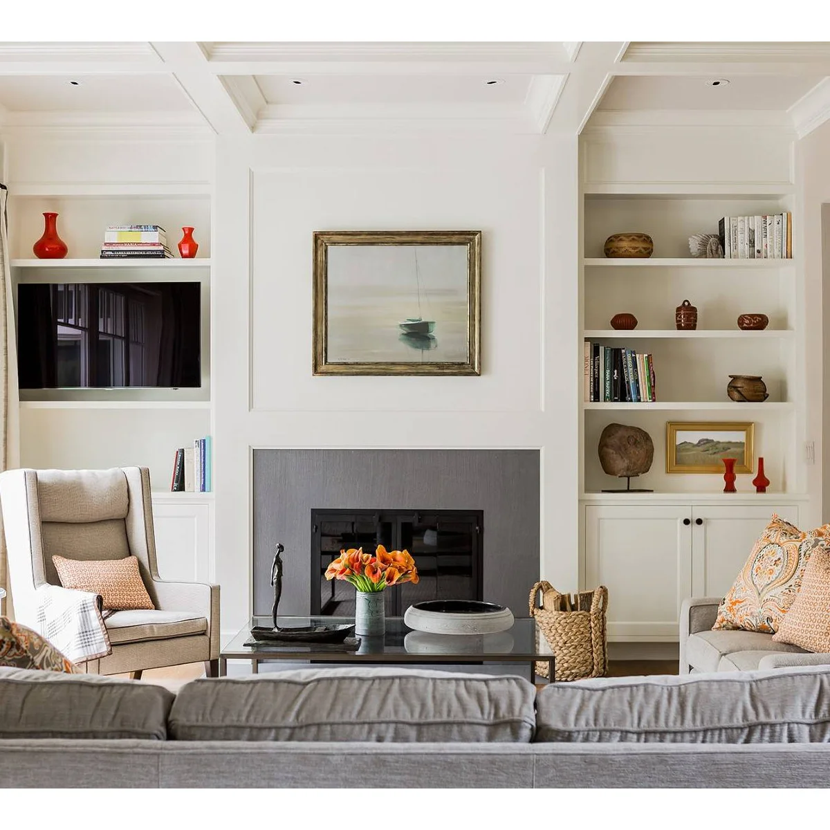 Red vessels and stacked books on a shelf immediately above a television in white cabinetry beside a fireplace.