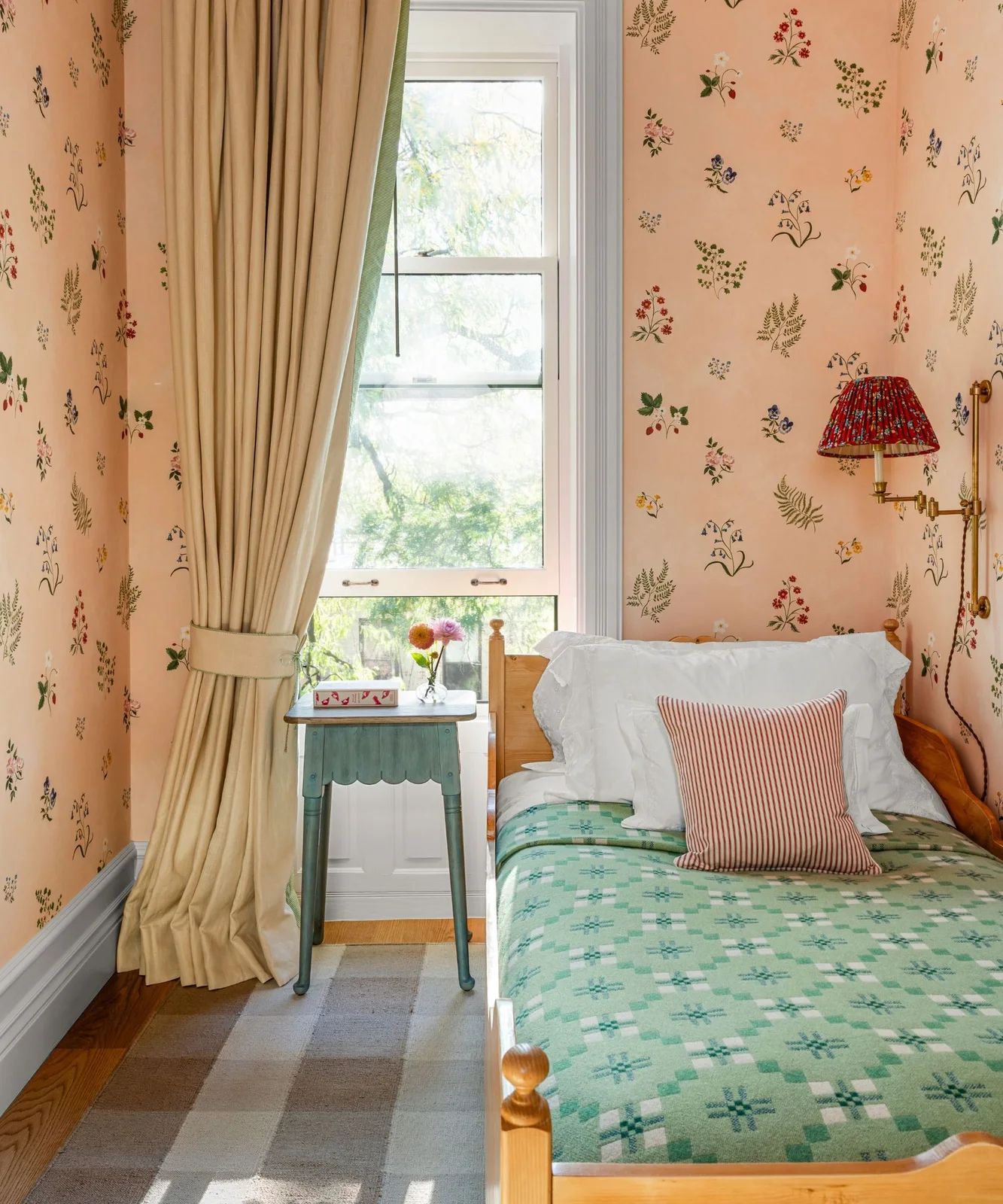 Small colored flowers repeat across peach-pink bedroom wallpaper around a timber bed and tall window.