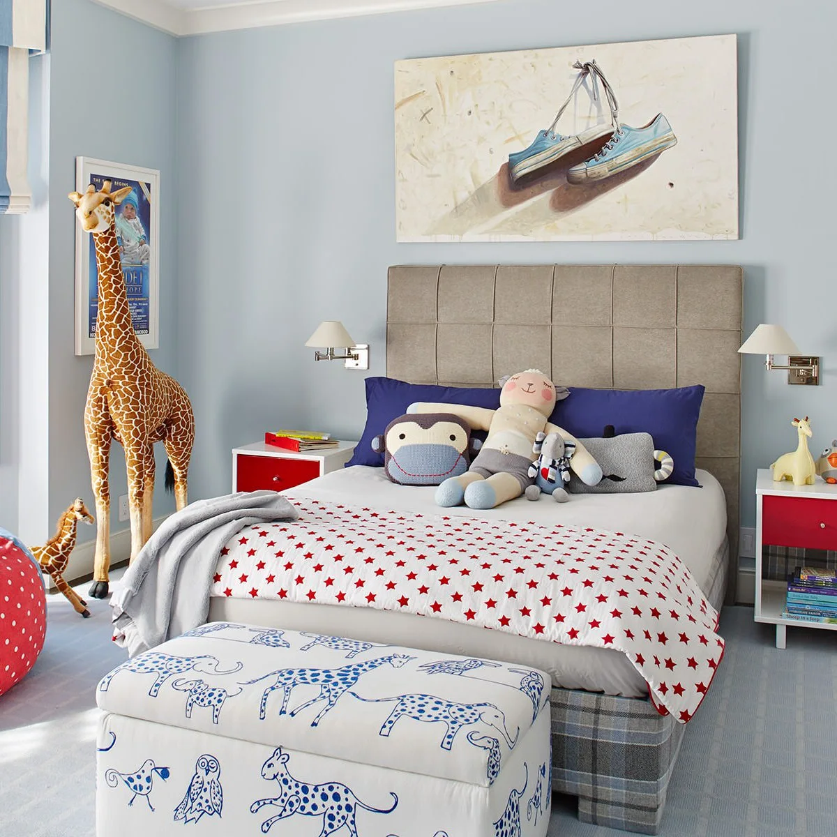 Pale blue boy’s bedroom with a gray upholstered headboard, animal-patterned bench and red-star bedding