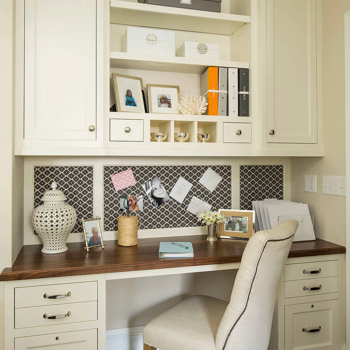 Wood-topped fitted desk with cream drawers and patterned noticeboard panels beneath overhead cabinets