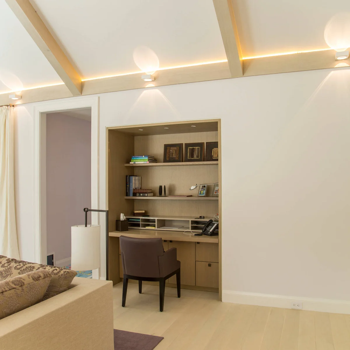 Recessed wood desk with shallow paper cubbies, shelves, a telephone and a brown chair beside a sofa