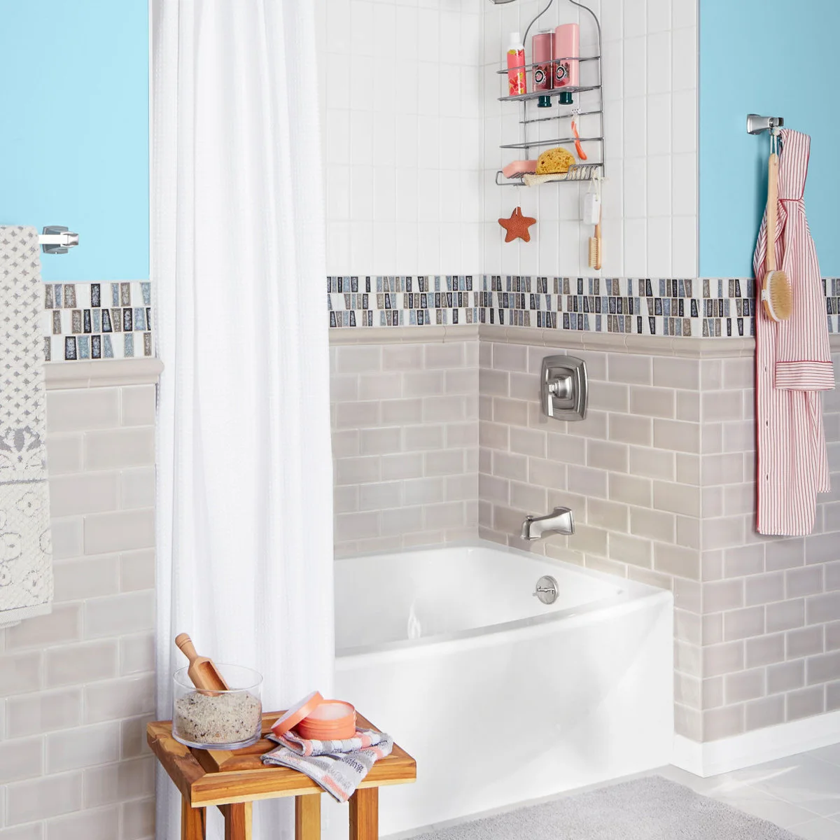 Plain white shower curtain beside a tiled tub, hanging shower caddy and blue upper walls.