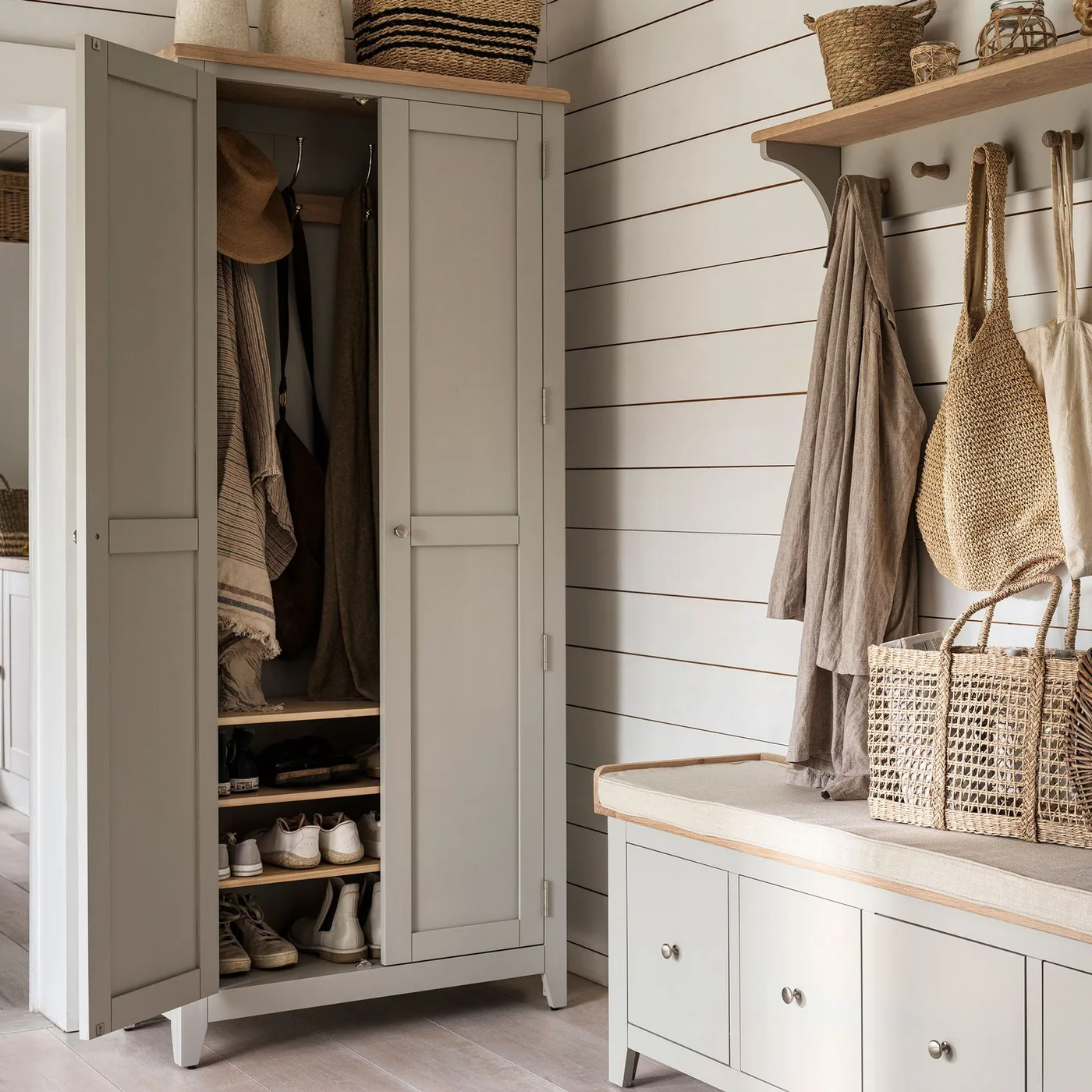 Entrance with pale gray cupboard, interior shoe shelves, matching storage bench, wooden shelf with hooks and white horizontal wall boards.
