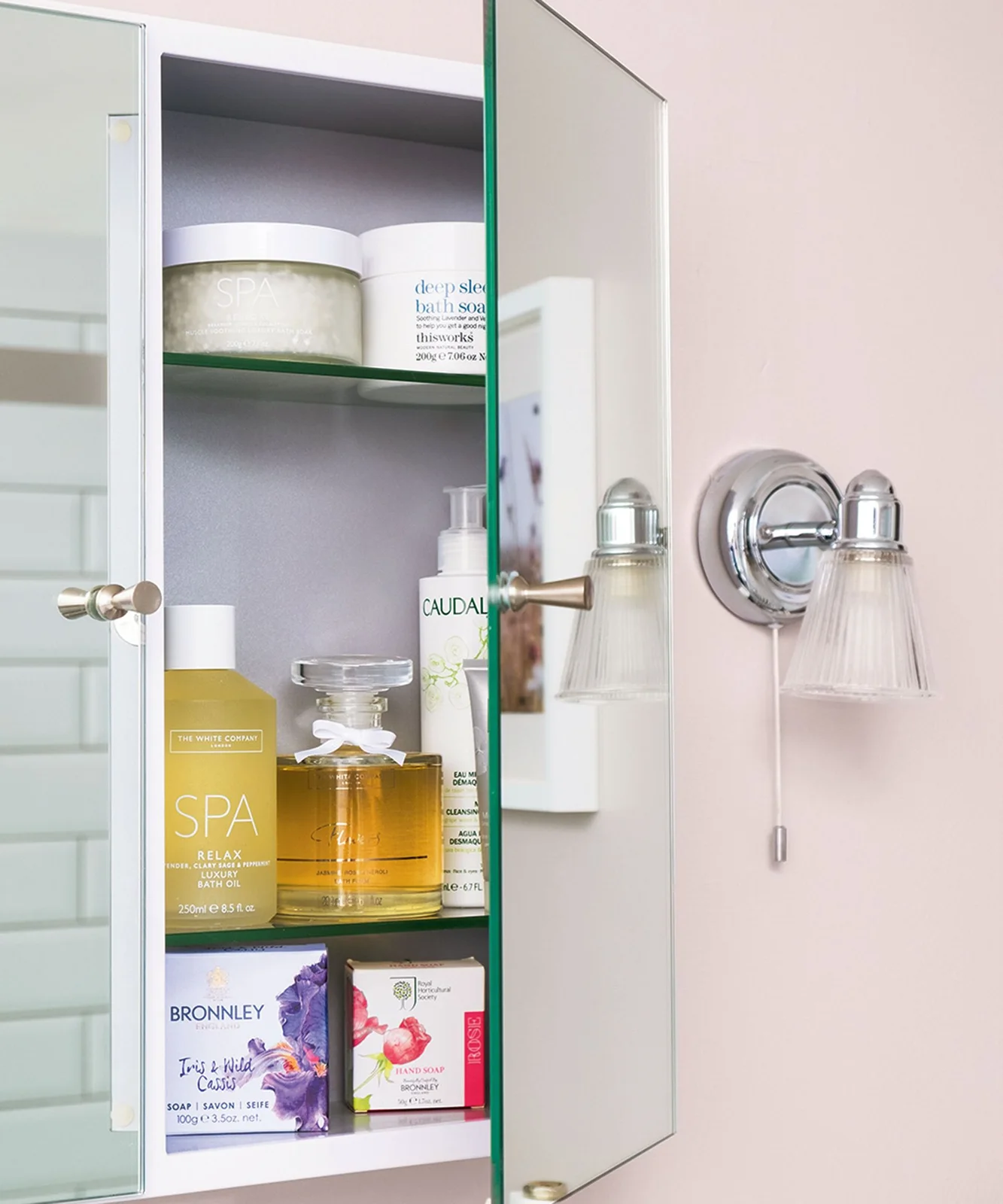 Open mirrored wall cabinet with glass shelves of bathroom toiletries
