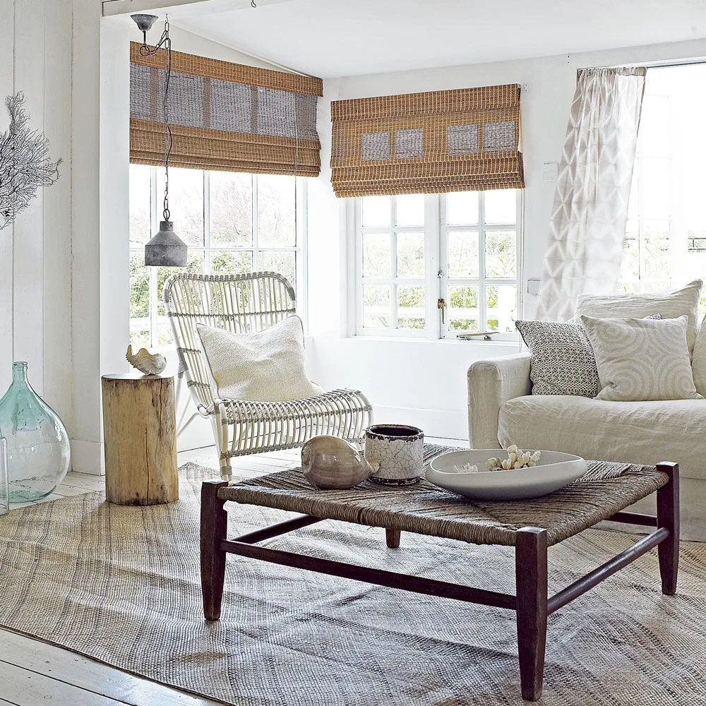 Pale sofa beside an open woven chair, woven-top coffee table and warm woven window shades