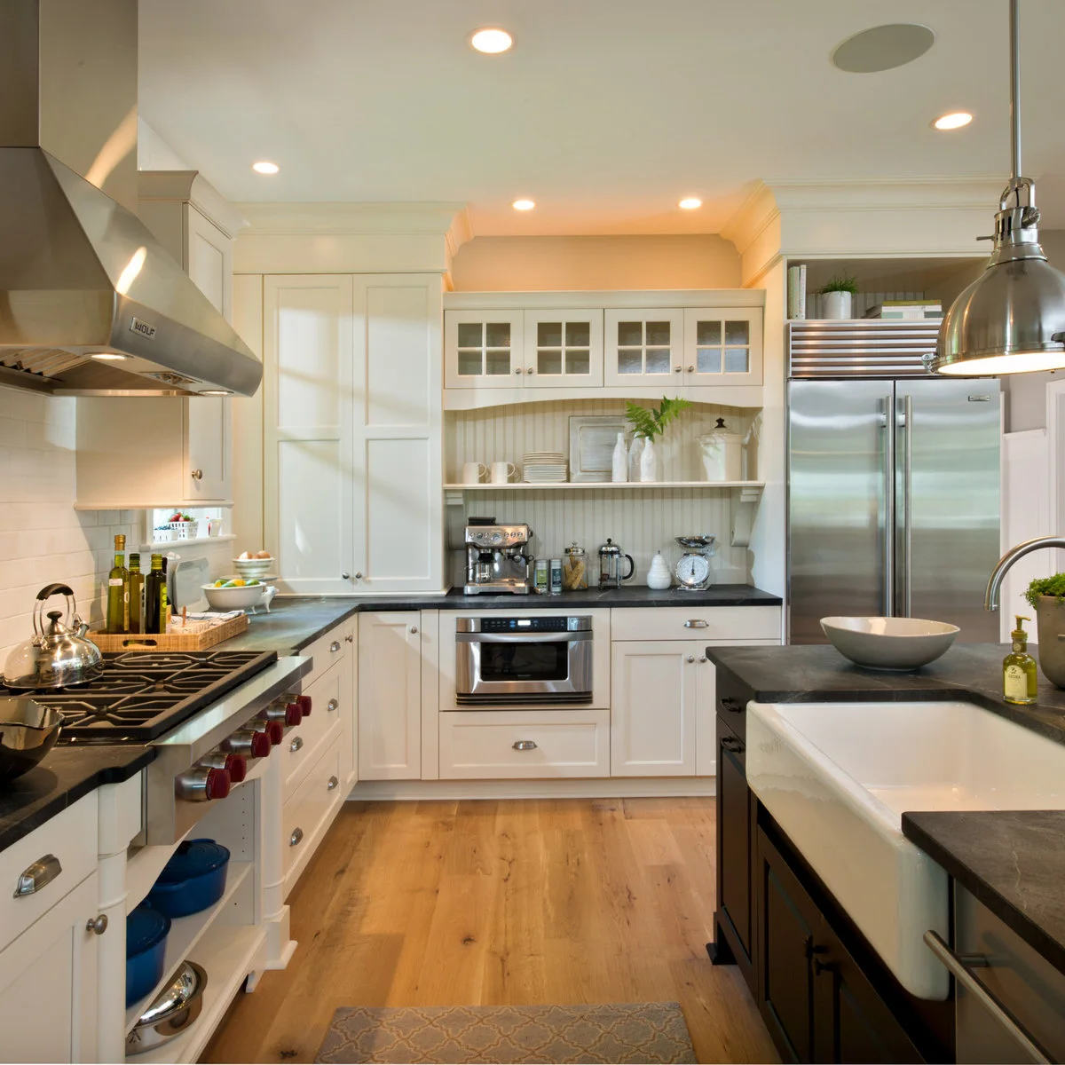A white apron-front island sink beneath a broad metal pendant, with an open view across the kitchen.