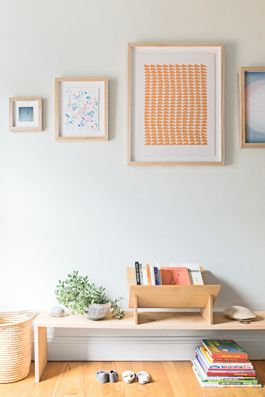 A low timber ledge holds a small book rack, plant and decorative objects beneath framed nursery artwork.