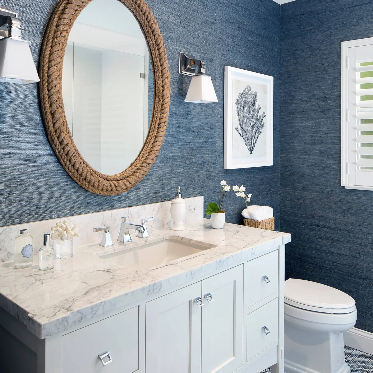 White vanity against blue walls with a white pump dispenser, small flowers and a white potted orchid.