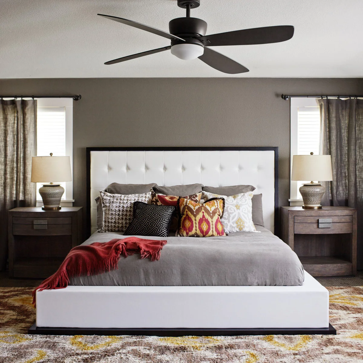 Grey bedding against a white headboard with patterned cushions, red throw and dark nightstands