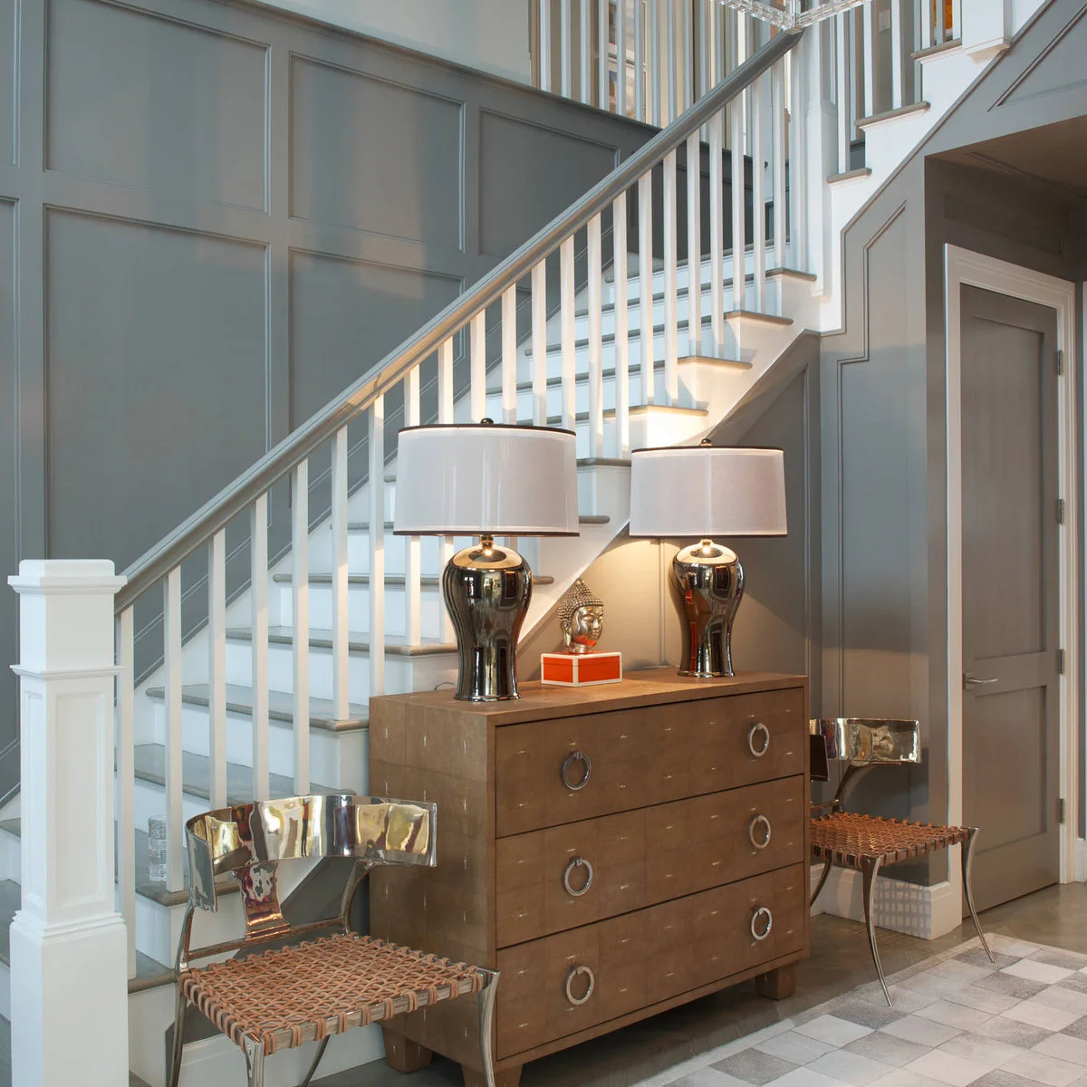 Gray painted wall molding frames a curved stair with white balusters and a wood chest below.