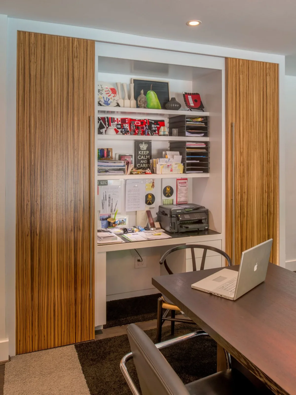 Wood-front sliding panels reveal a compact white desk and shelves filled with stationery, paper trays and a printer beside a dining table.