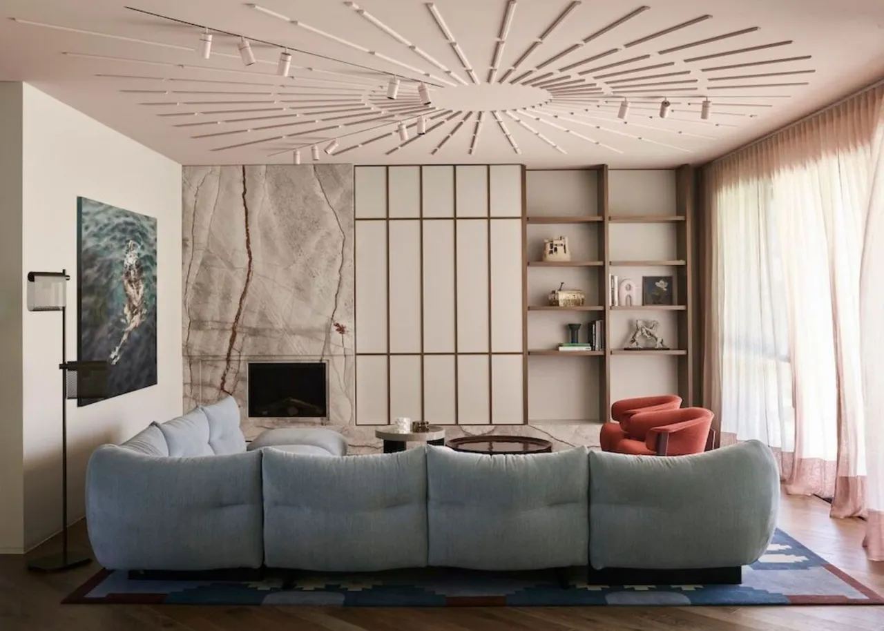 A pale blue sofa faces a quiet fireplace wall beneath a decorative ceiling.