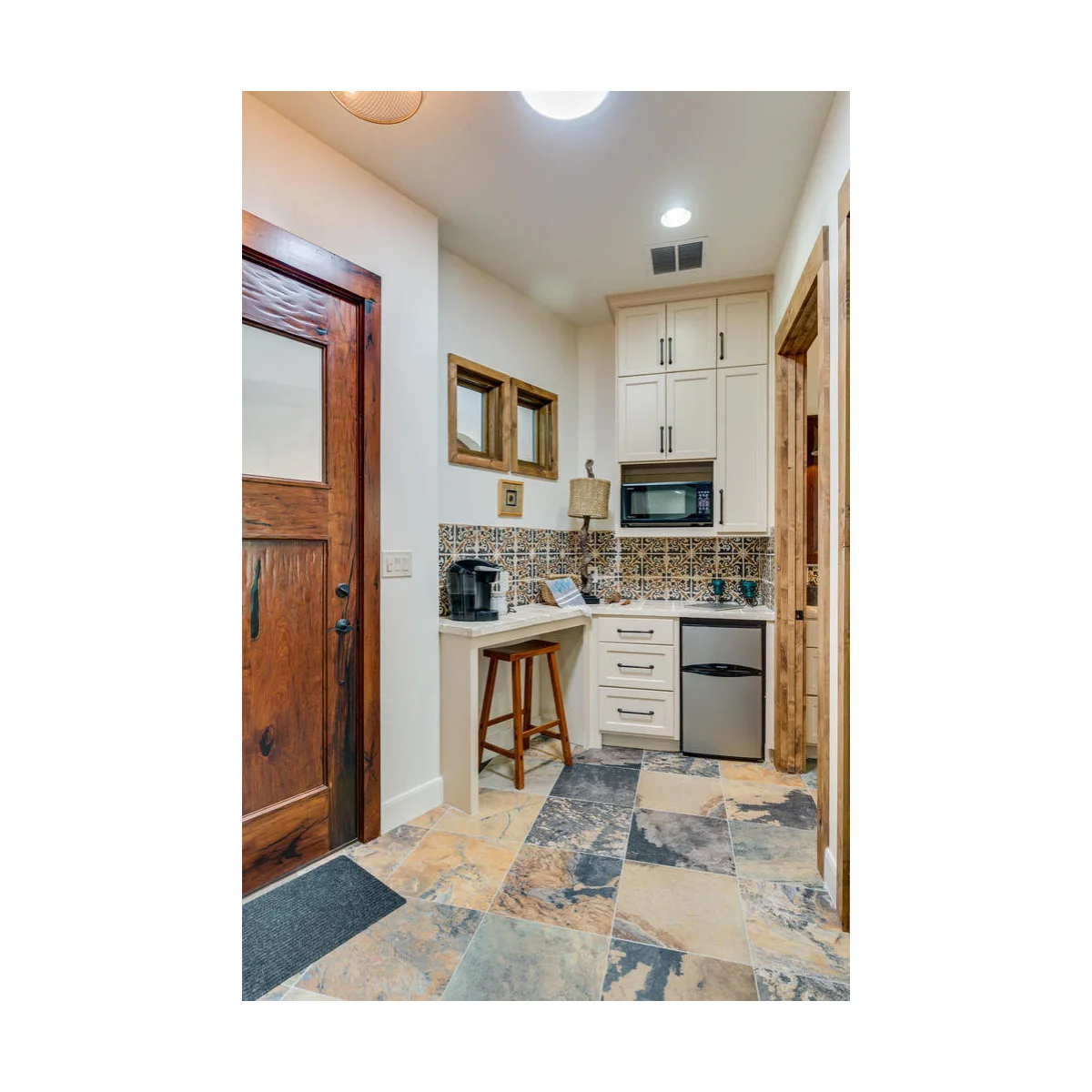 Compact white corner kitchenette with a microwave, small refrigerator and a stool under the return counter