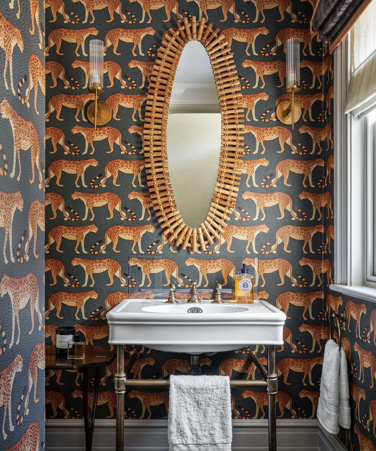 An illustrated dark wallpaper surrounds a compact basin below a woven-framed mirror.