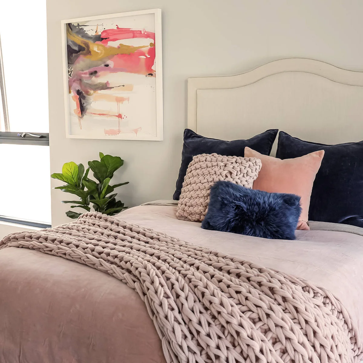 Teen bedroom with pale pink bedding, navy pillows and a chunky pale throw beneath abstract art