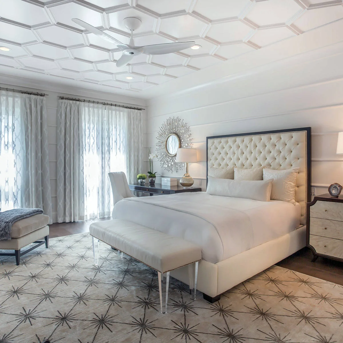 A pale tufted bed with a dressing desk and chair on one side and a drawer chest on the other.
