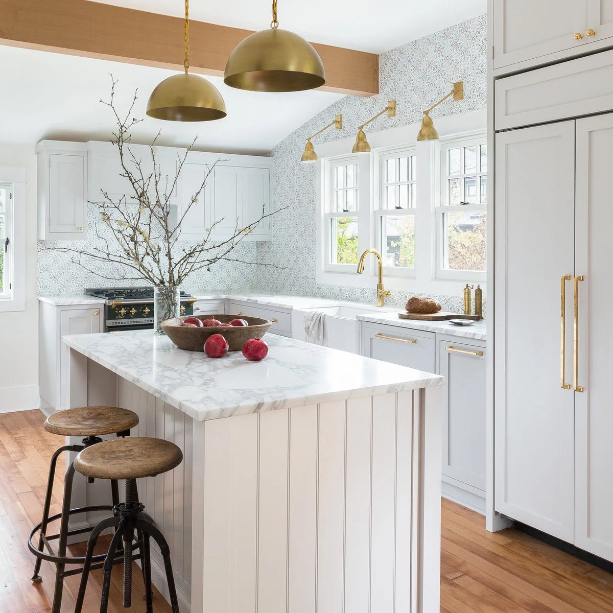 Warm metal dome pendants hang beside a wood beam, while small warm metal wall lights repeat above windows on a sloping tiled wall.