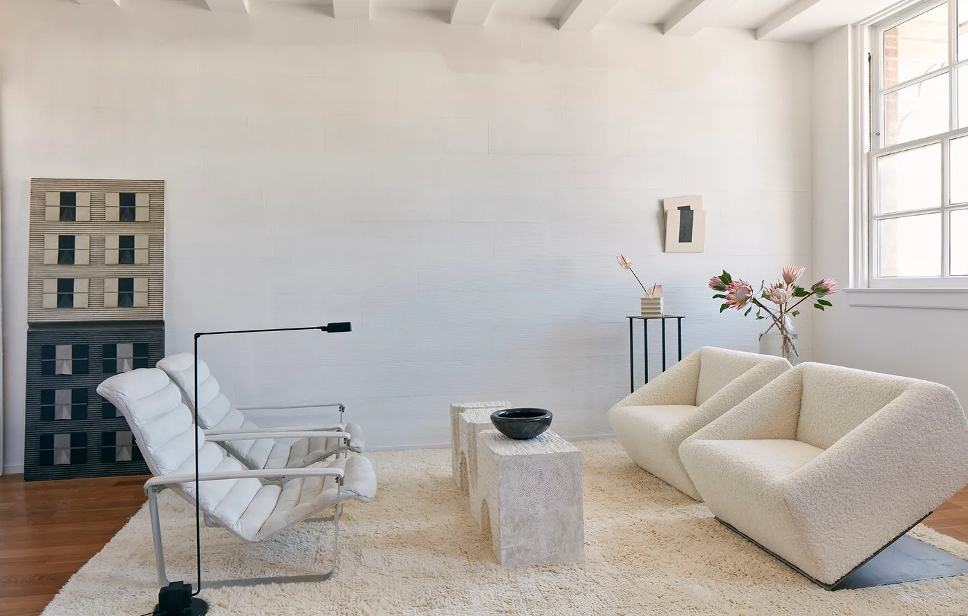 Pale angular armchairs facing two light framed lounge chairs across a narrow table on a warm wood floor