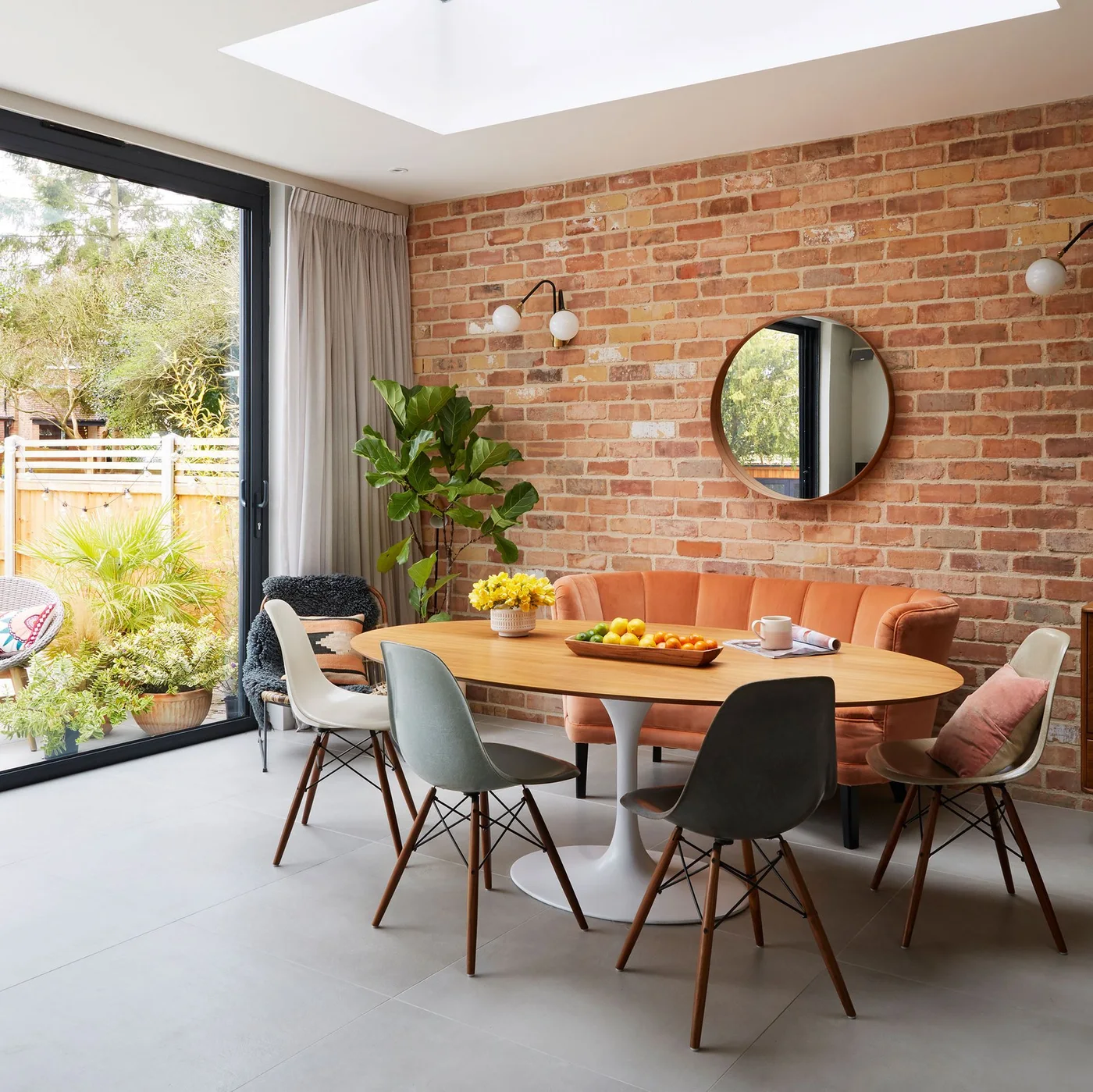 Round mirror above an orange upholstered breakfast seat against a brick wall with globe wall lights.