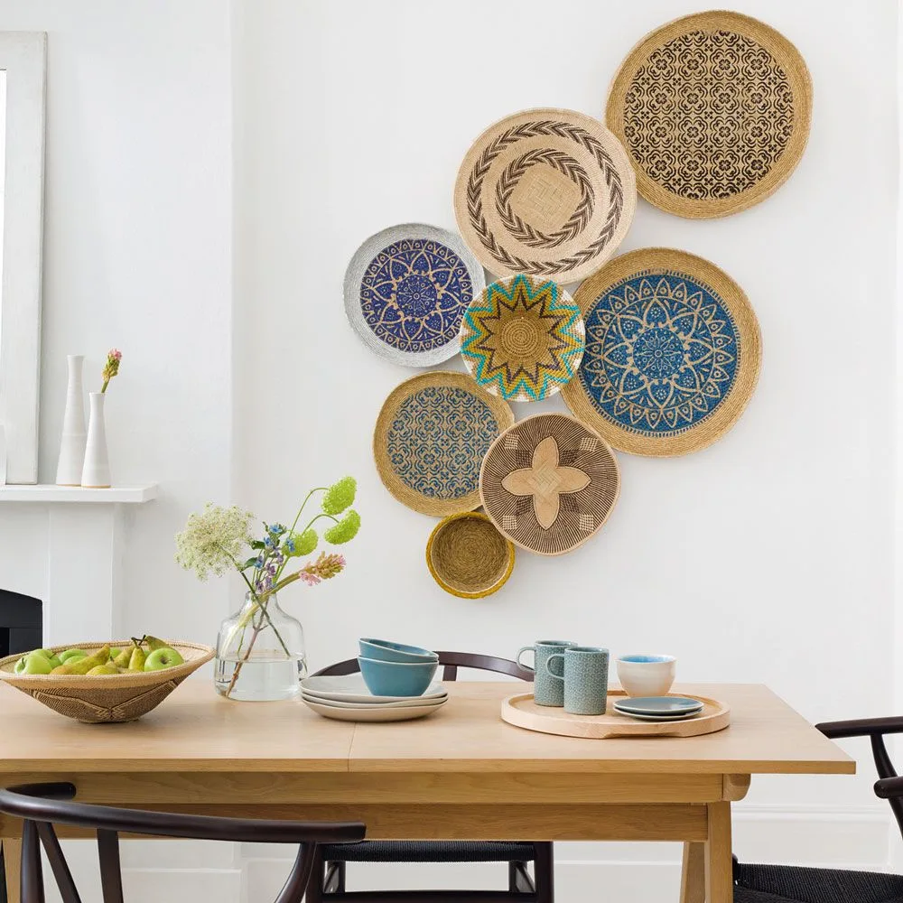 Round woven wall pieces with blue, green, and brown patterns clustered on a white wall beside a wooden dining table and black chairs.