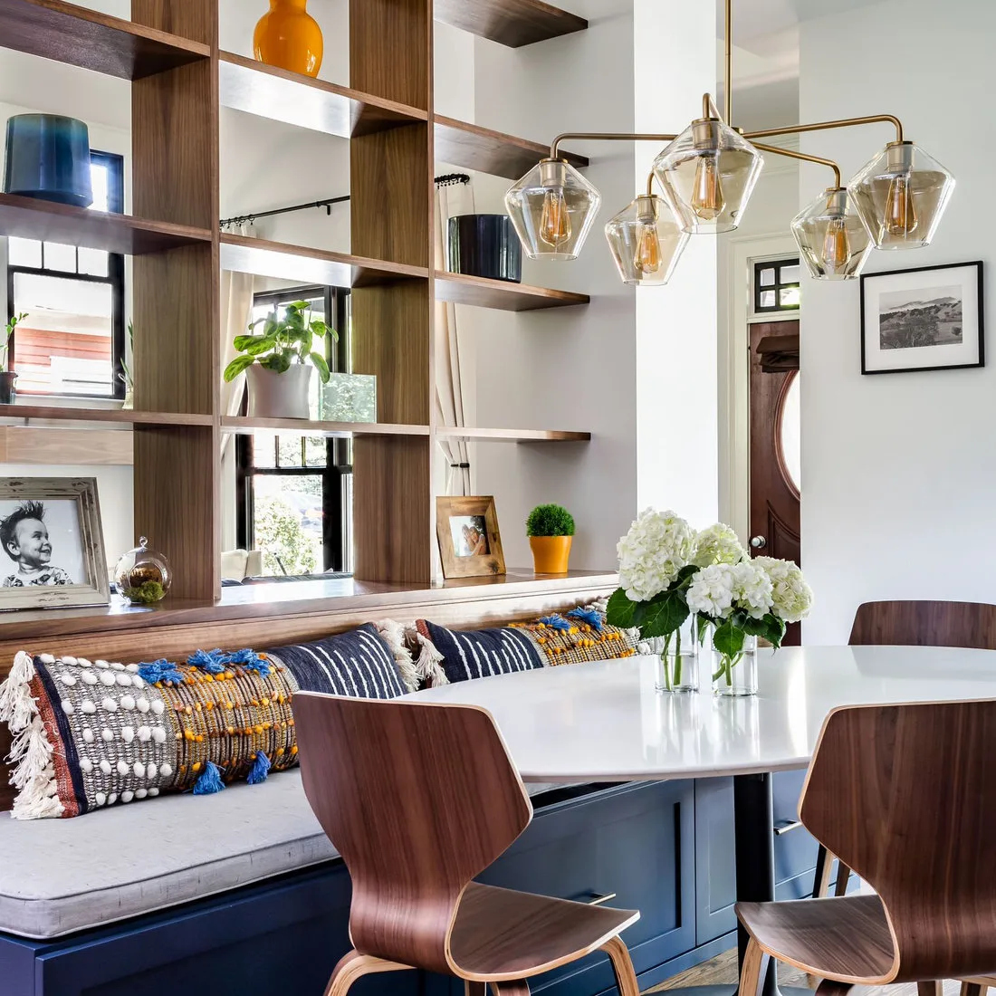 Open wood grid shelving above a blue dining bench with patterned cushions and curved wood chairs