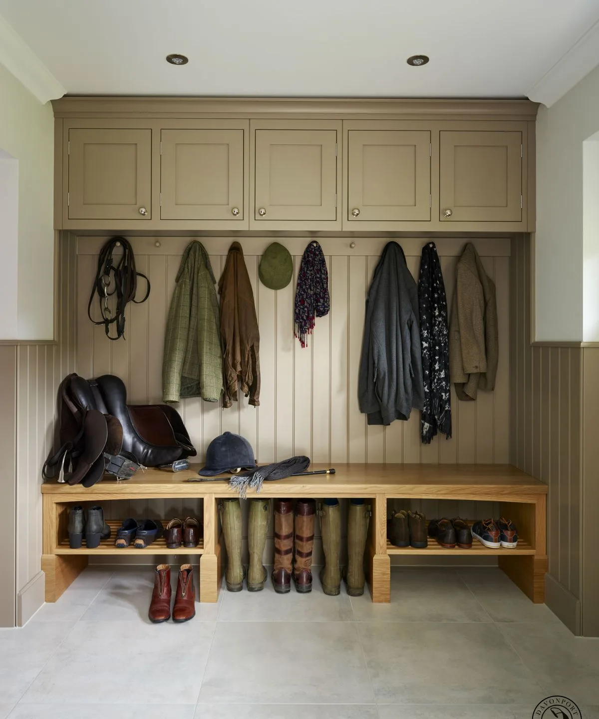 Olive-toned mudroom cupboards and coat hooks above a wooden bench with open boot shelves below.