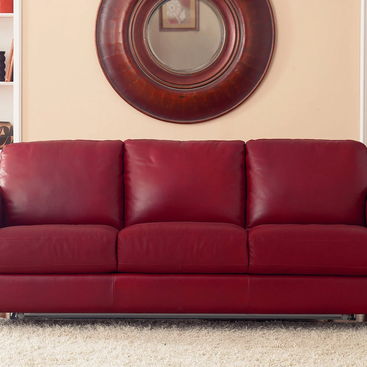 Red upholstered sleeper sofa with straight sides beneath a large round mirror