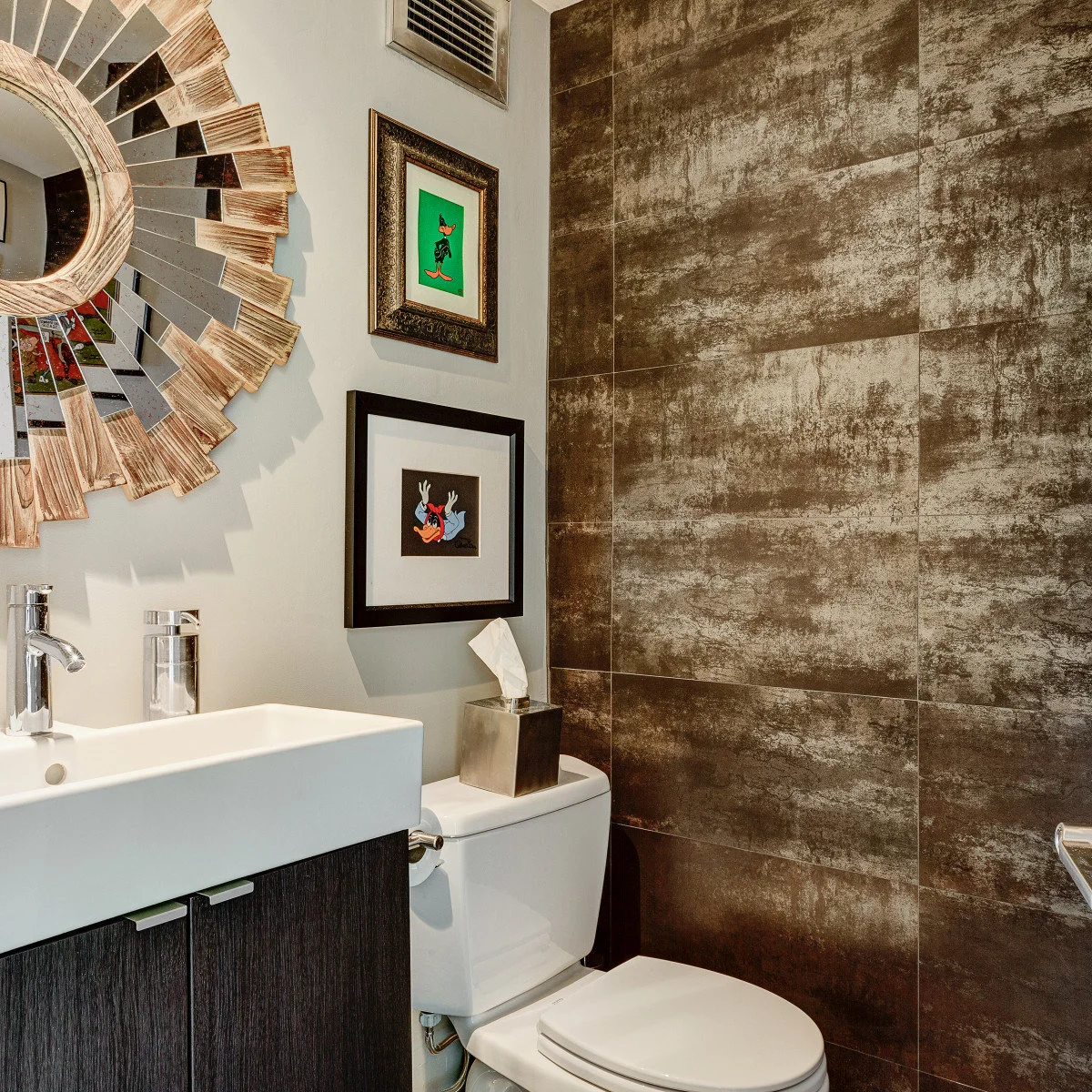 Two colorful cartoon prints beside a sunburst mirror in a compact bathroom