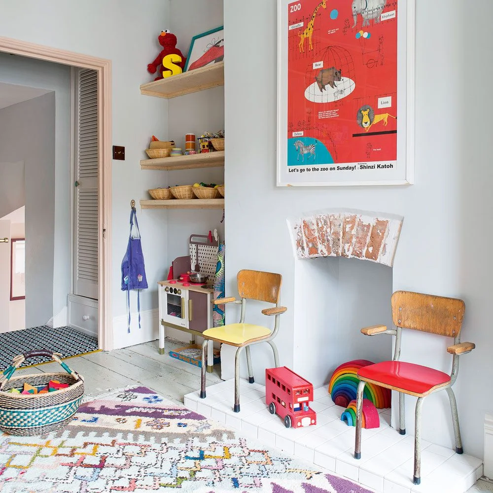 Play kitchen in an alcove with wood shelves and small baskets of pretend-play food and accessories