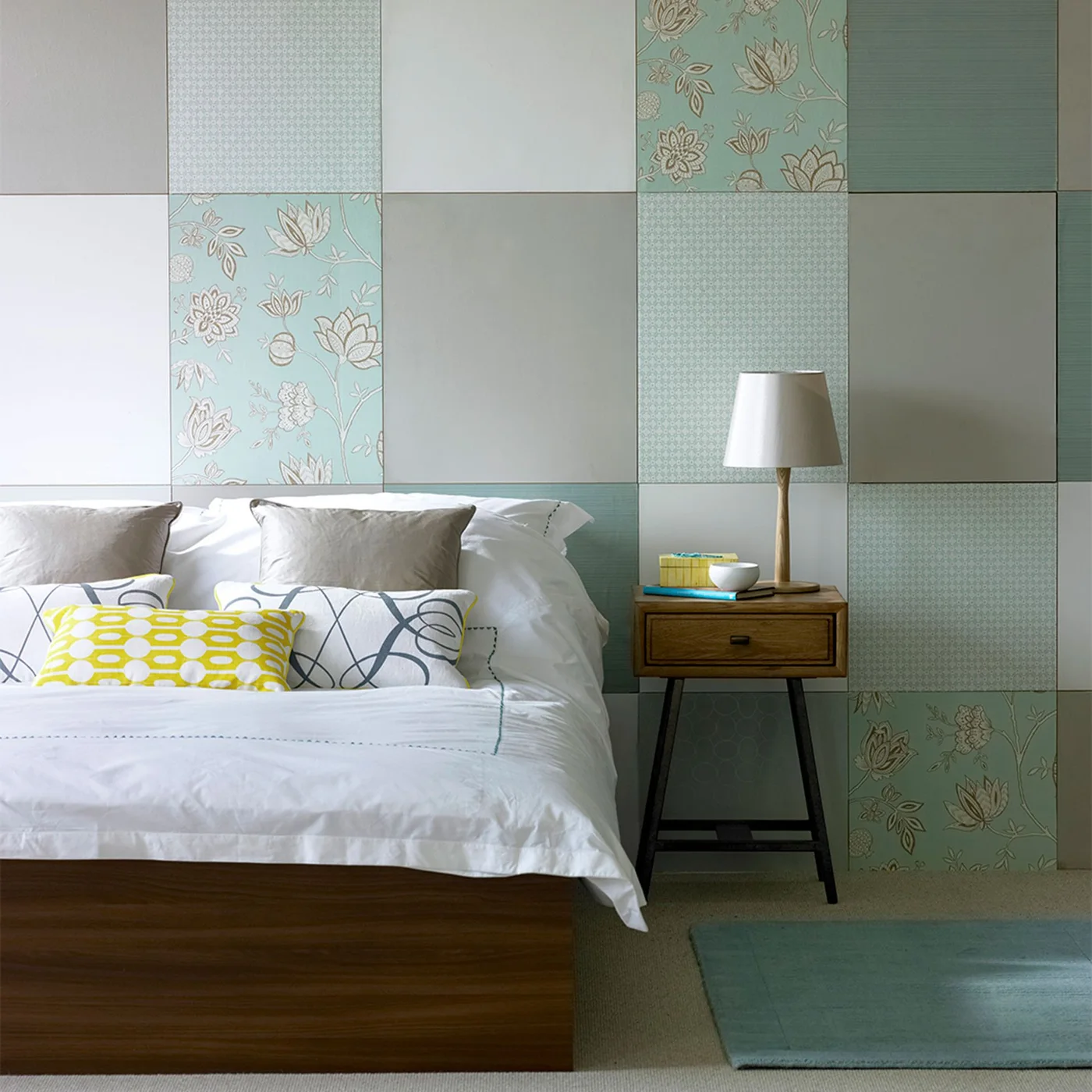 Pale green and neutral square wall panels with floral and small patterns sit behind white bedding and a wooden bedside table