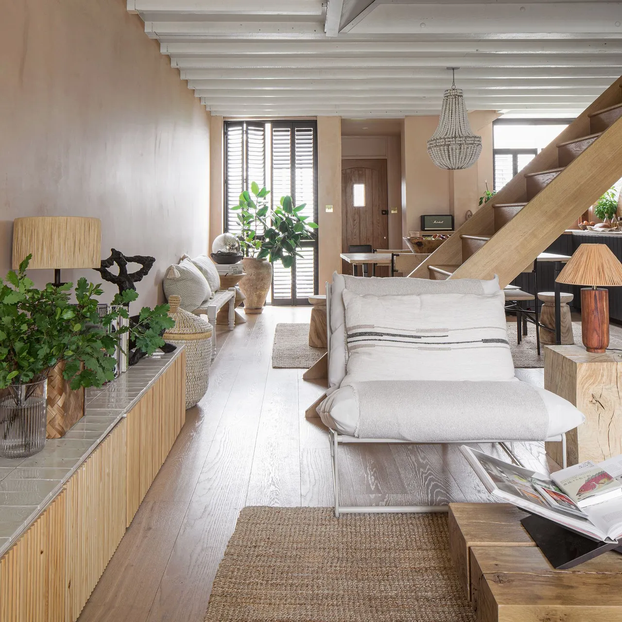 Pale armchairs sit beside a long timber media unit beneath light ceiling beams.