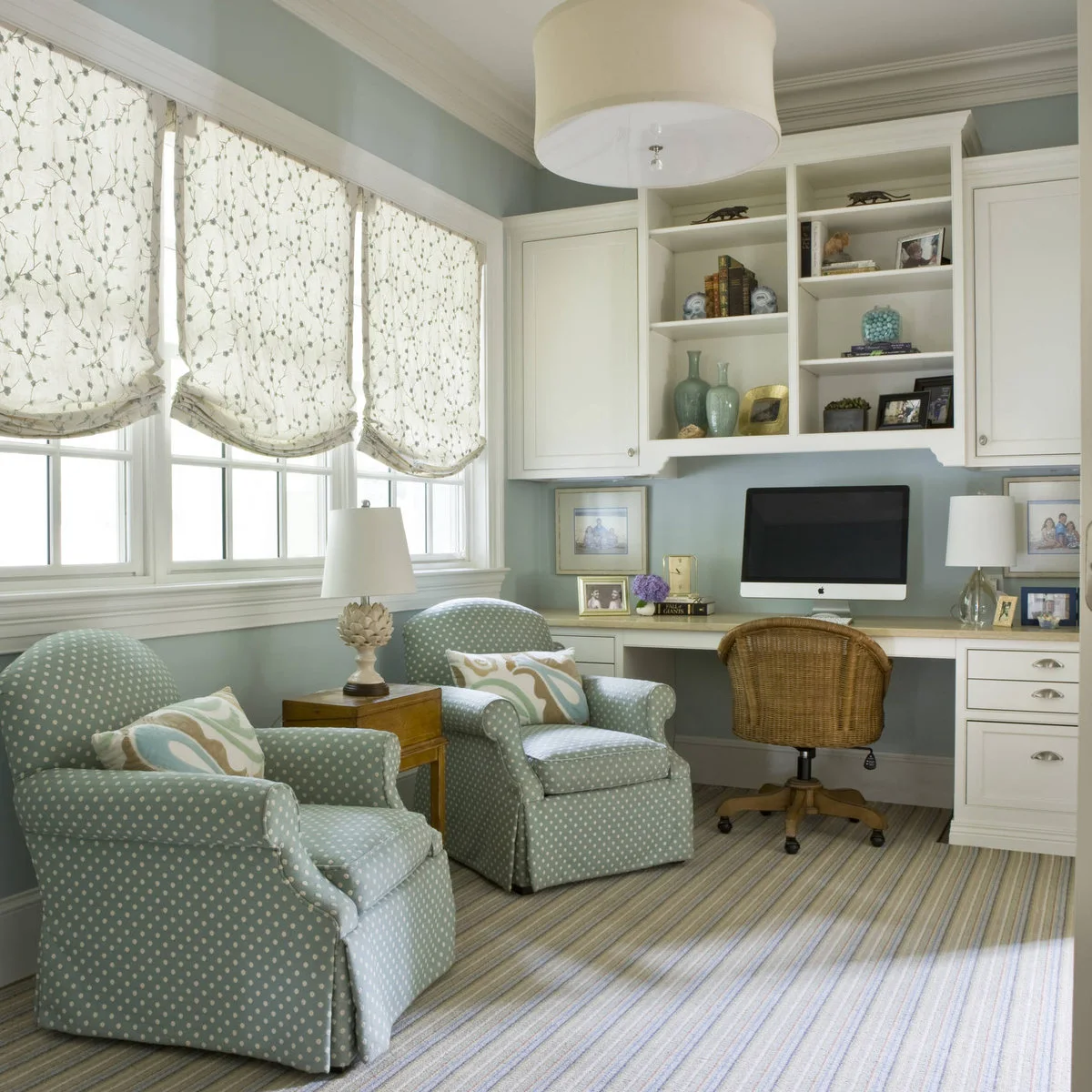 Pale blue home office with white built-in desk, two patterned blue armchairs and fabric window shades