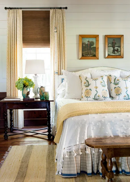 Floral pillows sit on pale bedding beside a timber nightstand and bright window.